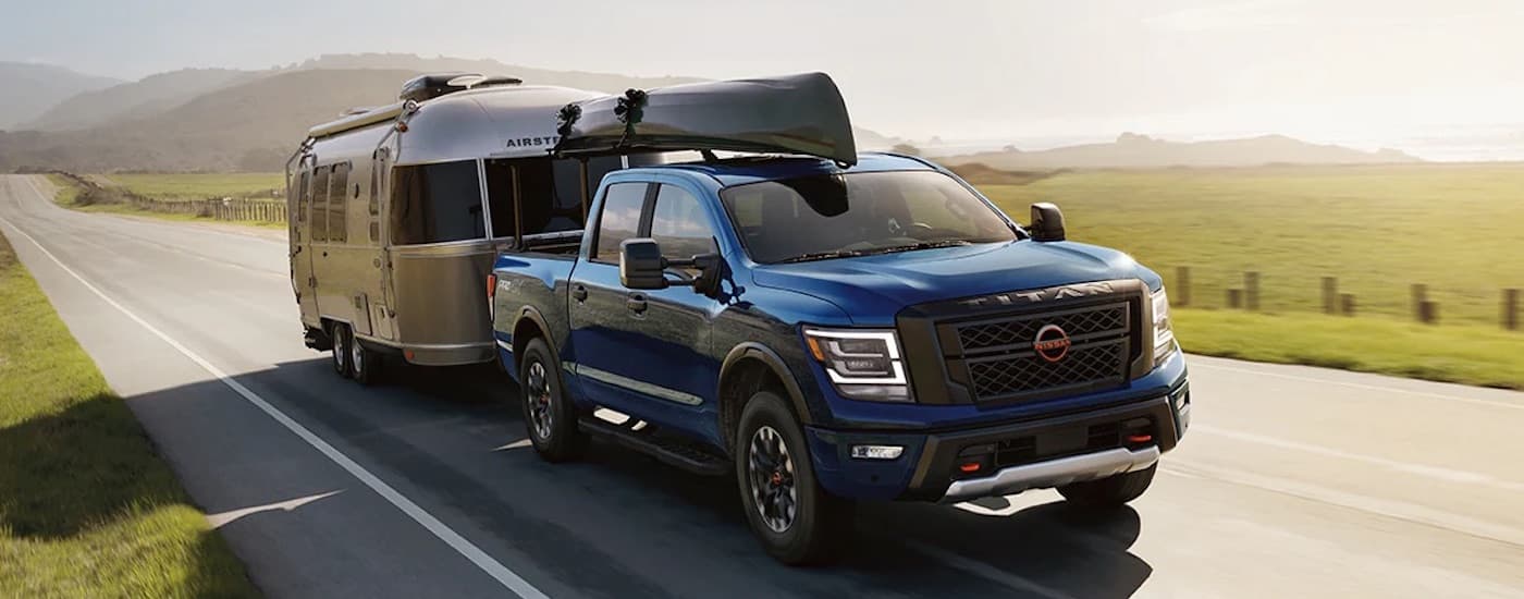 A blue 2024 Nissan Titan is shown from the front at an angle while towing a camper.