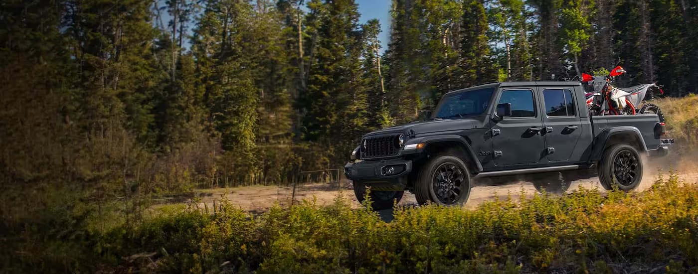 A dark grey 2024 Jeep Gladiator Nighthawk is off-roading on a dusty trail.
