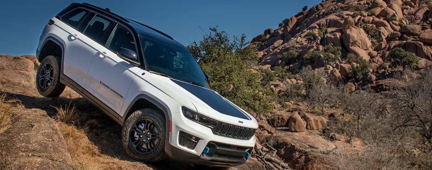 A white 2024 Jeep Grand Cherokee 4xe is off-roading on a steep trail.