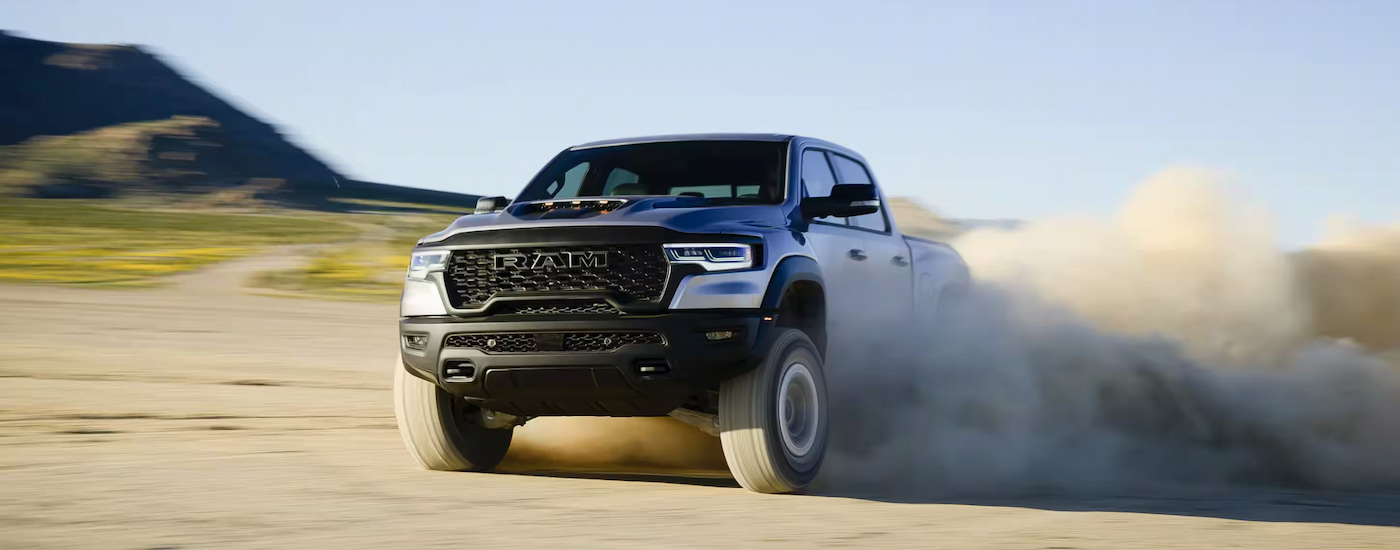 A white 2025 Ram 1500 RHO spinning its wheels in dust while off-roading.