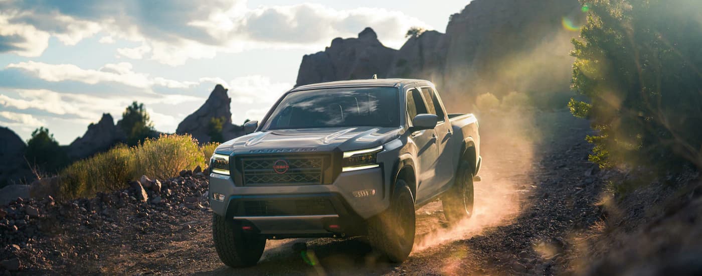 A grey 2023 Nissan Frontier PRO-4x is driving on a dusty dirt road.