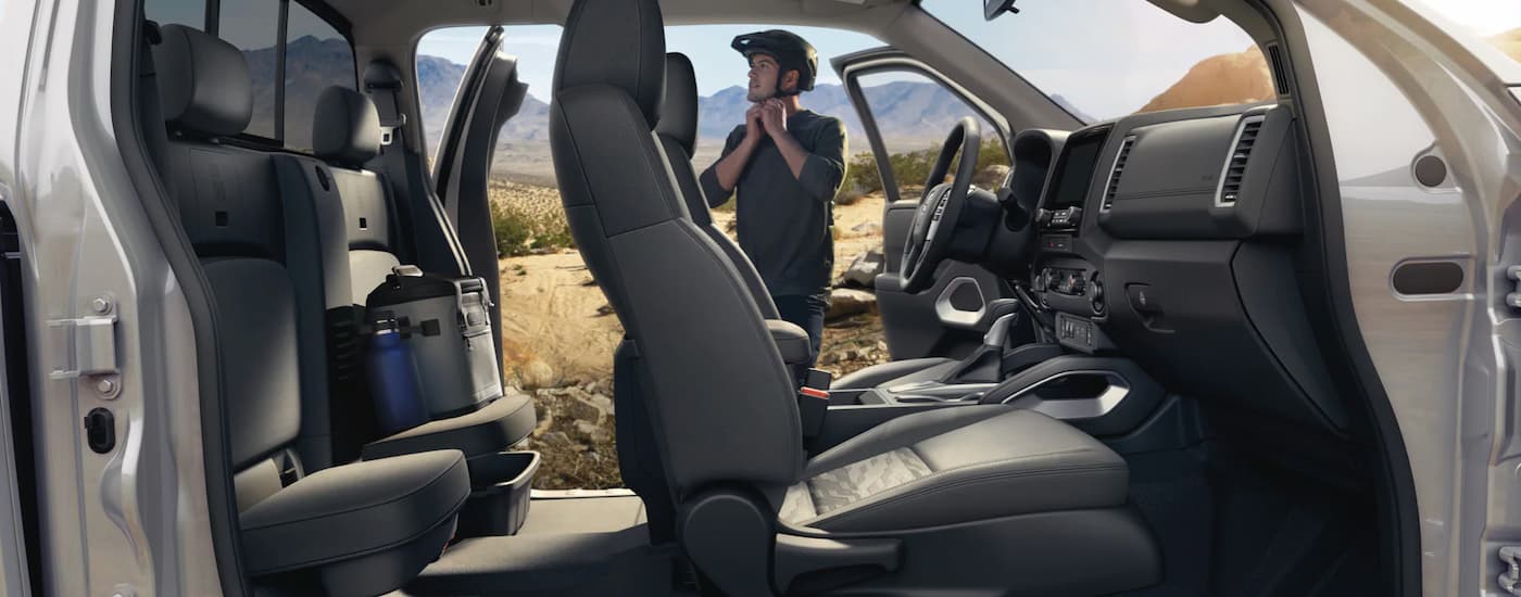 A man is standing next to a 2023 Nissan Frontier PRO-4x that's parked with the doors open.