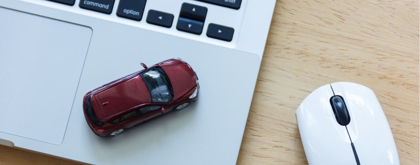 A red toy car is on top of a laptop on a desk.