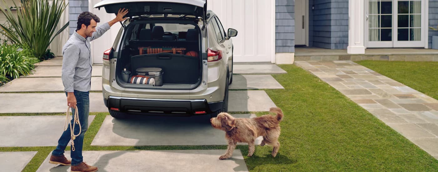 A man is opening the rear cargo door of a tan 2025 Nissan Rogue Platinum.