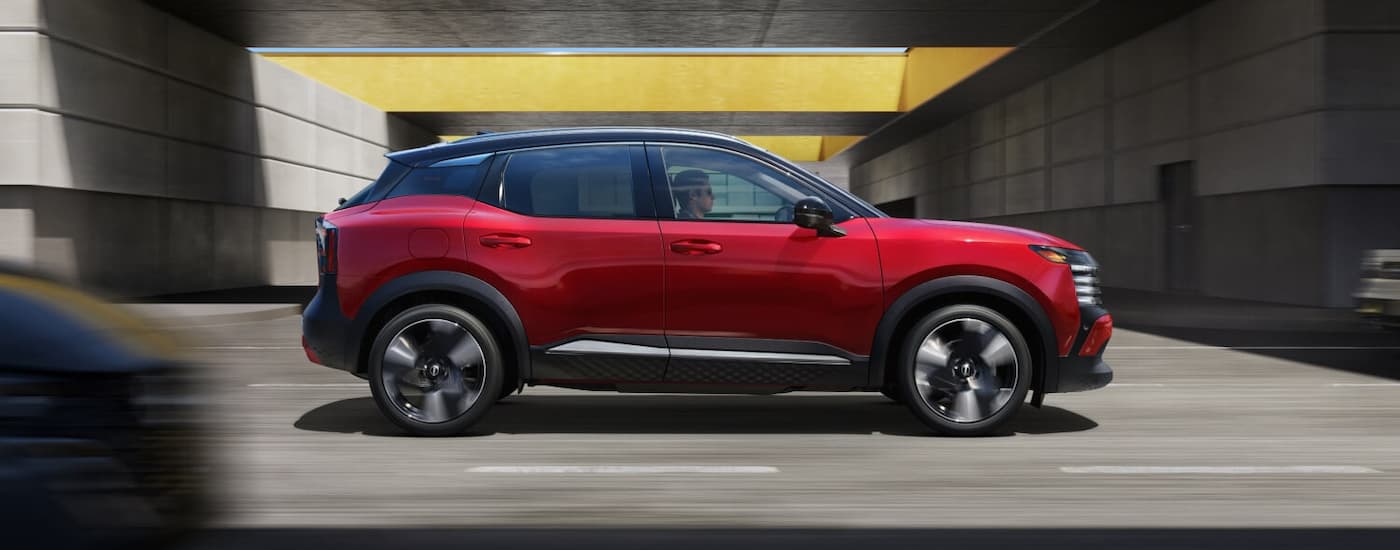 A red 2025 Nissan Kicks is driving on a city street.
