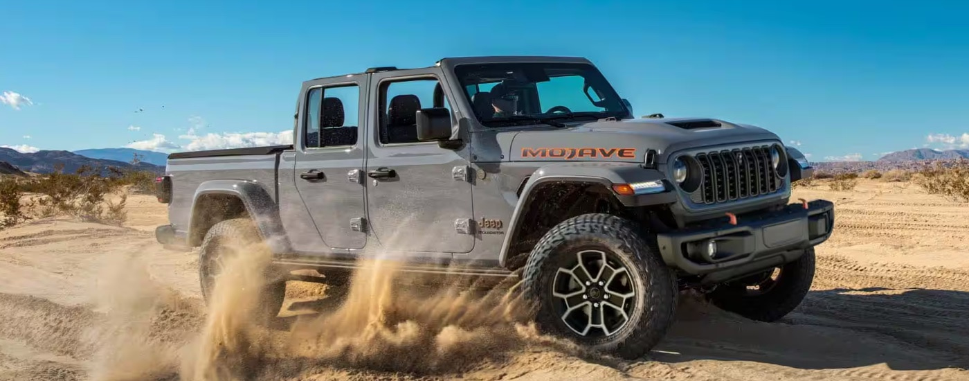 A grey 2024 Jeep Gladiator Mojave kicking up sand while off-roading.