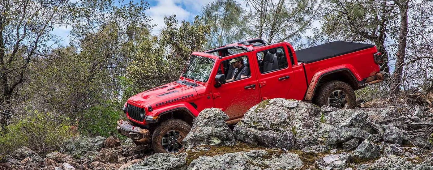 A red 2024 Jeep Gladiator Rubicon off-roading over large rocks.