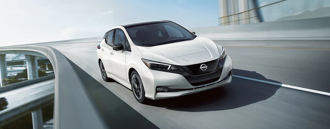 A white 2025 Nissan Leaf SV Plus is driving on a winding highway.