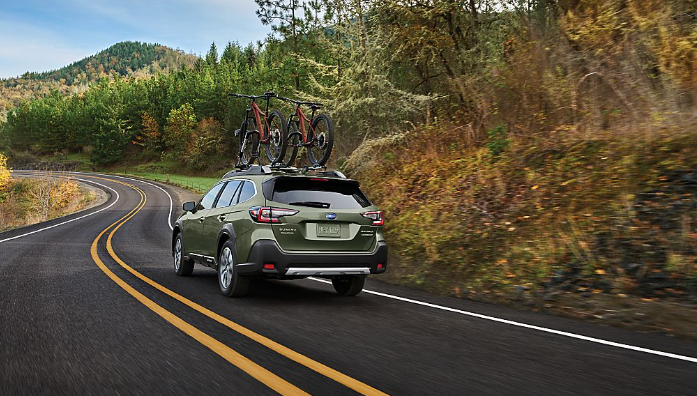 A 2025 Subaru Outback with two bikes on the roof drives through a curve on a rural two-lane highway