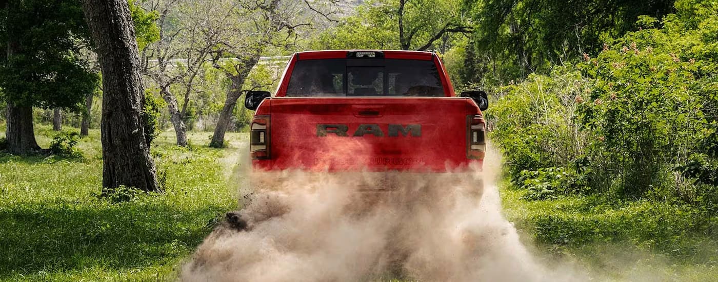 A red 2023 Ram 2500 Power Wagon is driving on a dusty dirt road lined with trees.