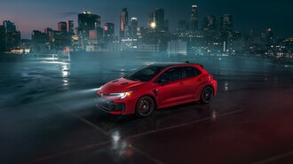A red GR Corolla driving in a parking lot at night with its headlights on.