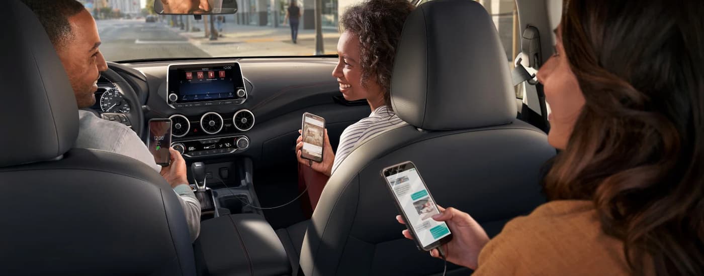 A group of friends are sitting in a parked in a 2024 Nissan Sentra in a city.