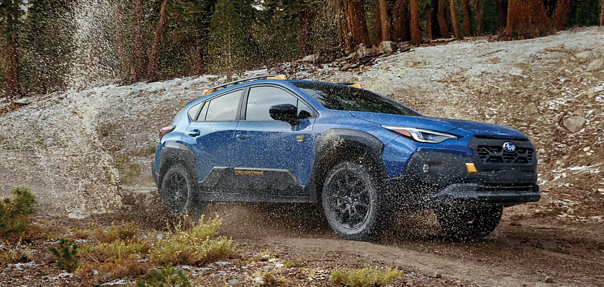 A blue 2024 Subau Crosstrek Wilderness fords a big puddle on a dirt trail