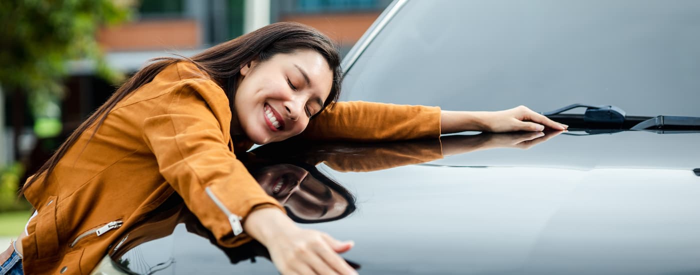 A woman is hugging the hood of a black vehicle after getting a subprime auto loan.