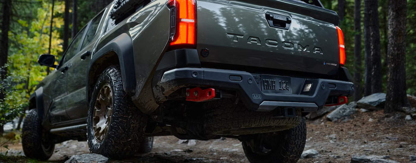 Rear view of a grey 2024 Toyota Tacoma Trailhunter parked off-road in the woods.