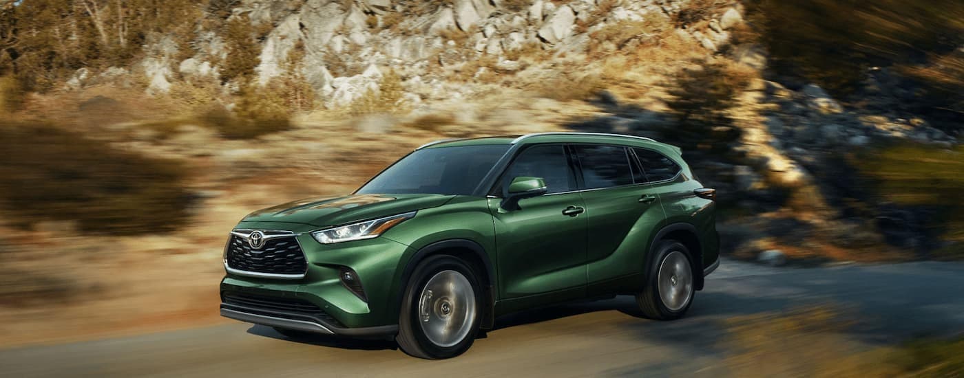 A green 2023 Toyota Highlander, a used car for sale, driving past cliffs.