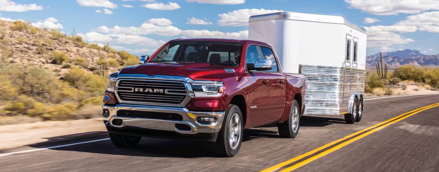 A red 2019 Ram 1500 Laramie towing a trailer on a highway.
