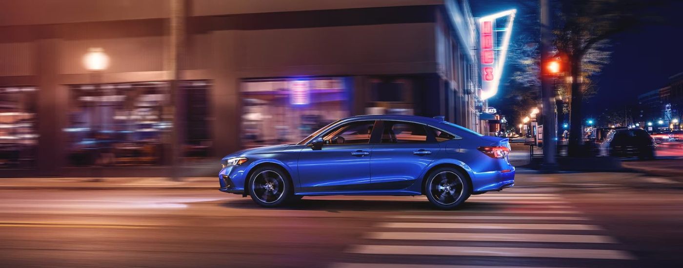 Side view of a blue 2023 Honda Civic Touring driving past neon city lights.