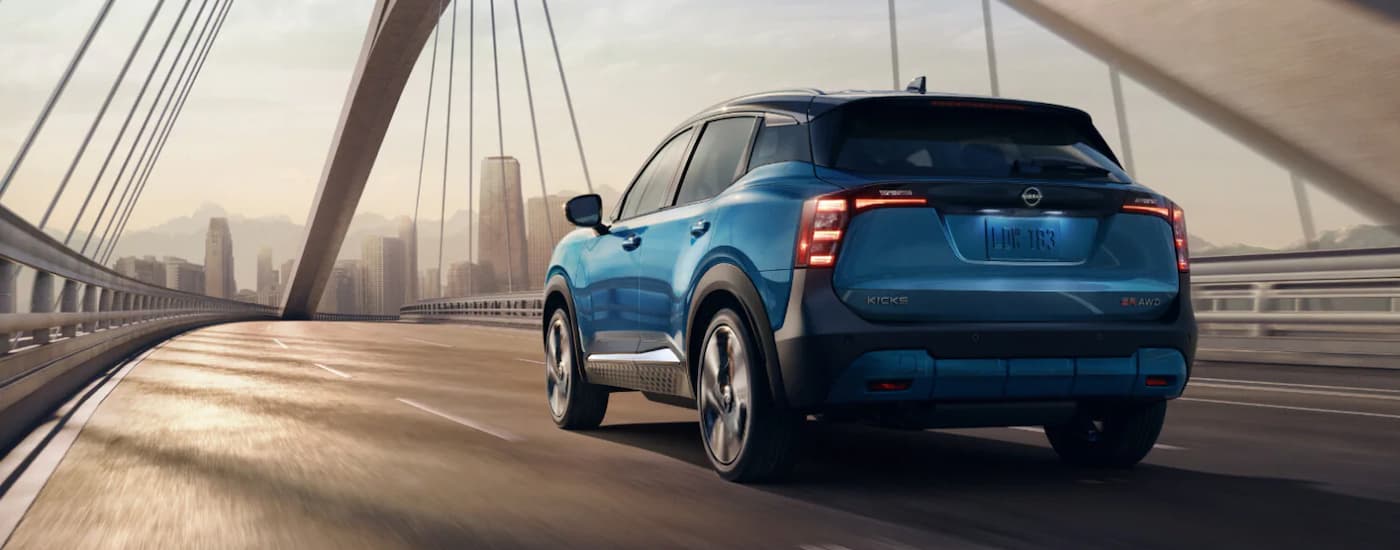 A blue 2025 Nissan Kicks SR is driving on a city bridge.