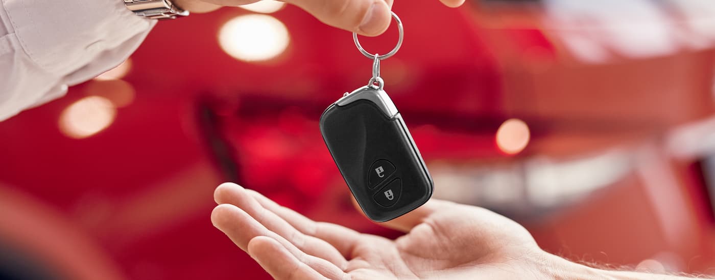A salesman is handing a car key to a customer.