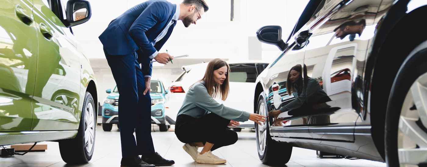 A woman is inspecting the tire of a vehicle while speaking to a salesman.