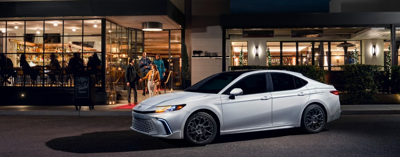 A white 2025 Toyota Camry for sale parked near a bar.