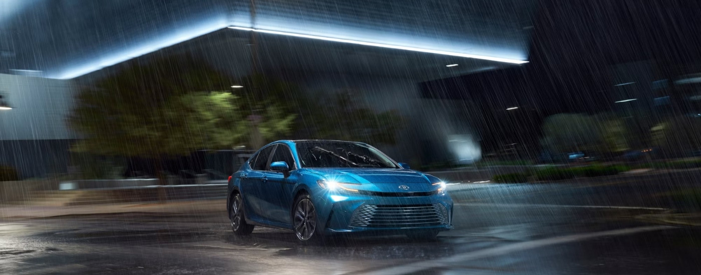 A blue 2025 Toyota Camry parked on a rainy night.