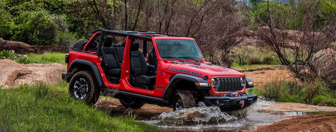 A red 2025 Jeep Wrangler Rubicon is driving through a river.