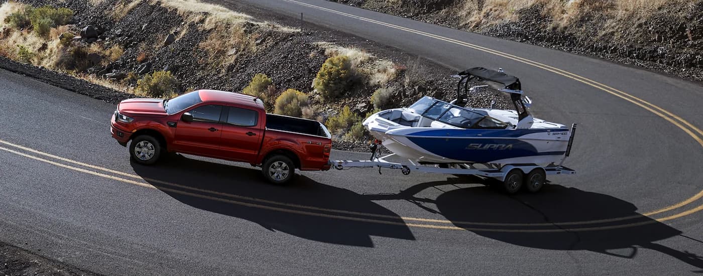 A red 2023 Ford Ranger XLT is towing a boat around a winding road.