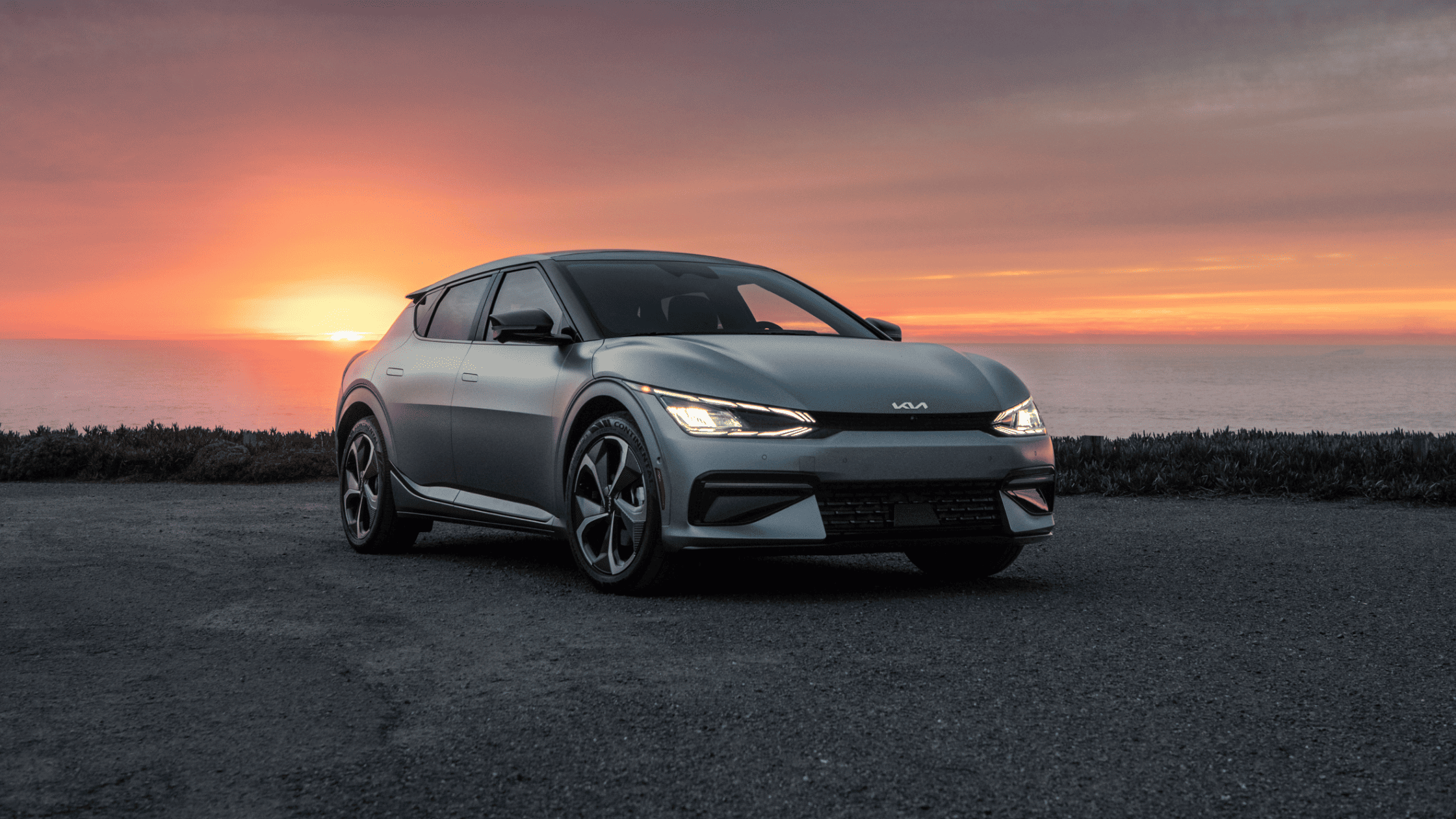 2024 Kia EV6 electric car parked by the coast with a vivid sunset view.
