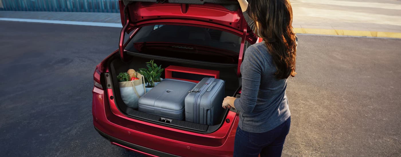 A woman is getting suitcases and groceries out of the trunk of a red 2025 Nissan Versa.