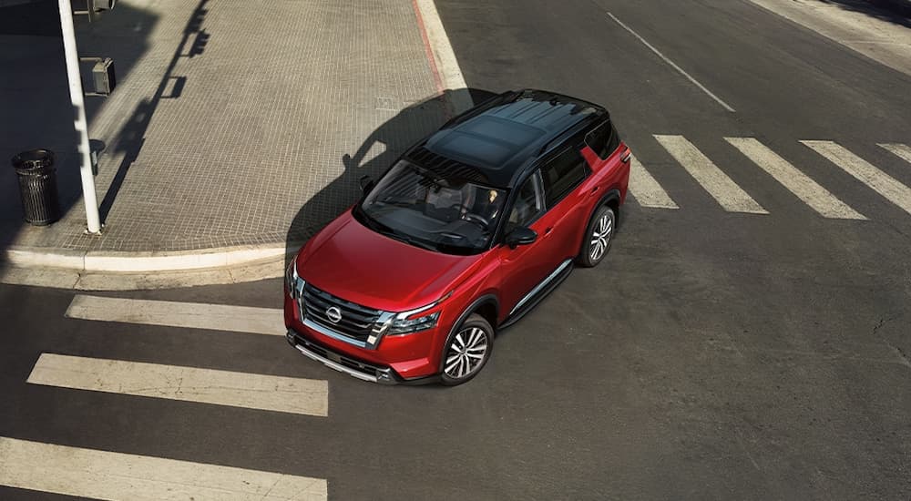 A red 2024 Nissan Pathfinder Platinum is driving on a city street during a test drive at a car dealer.