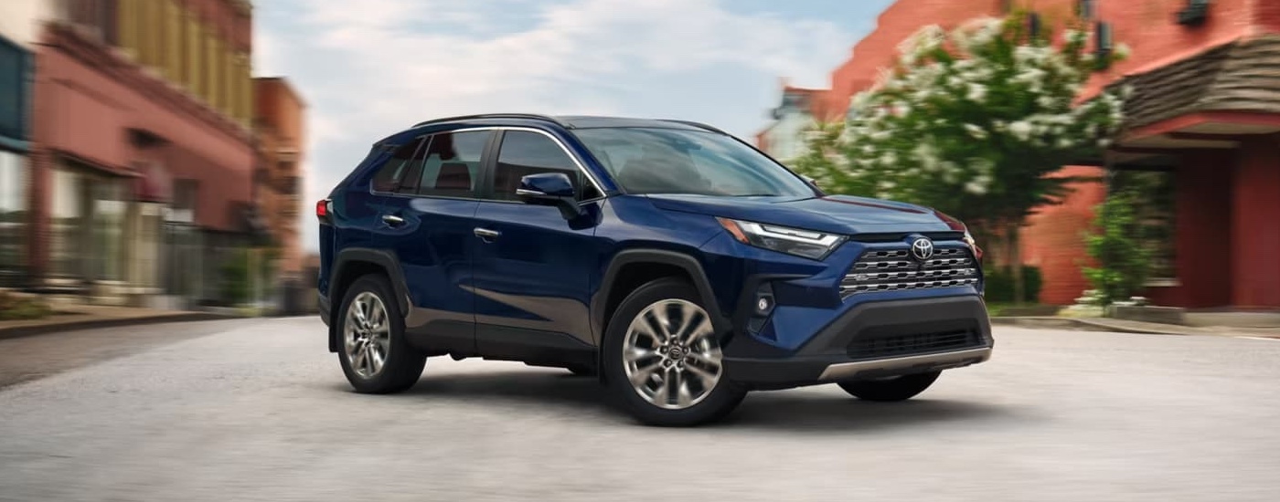 A black 2025 Toyota RAV4 Limited is driving on a road lined with brick shops.