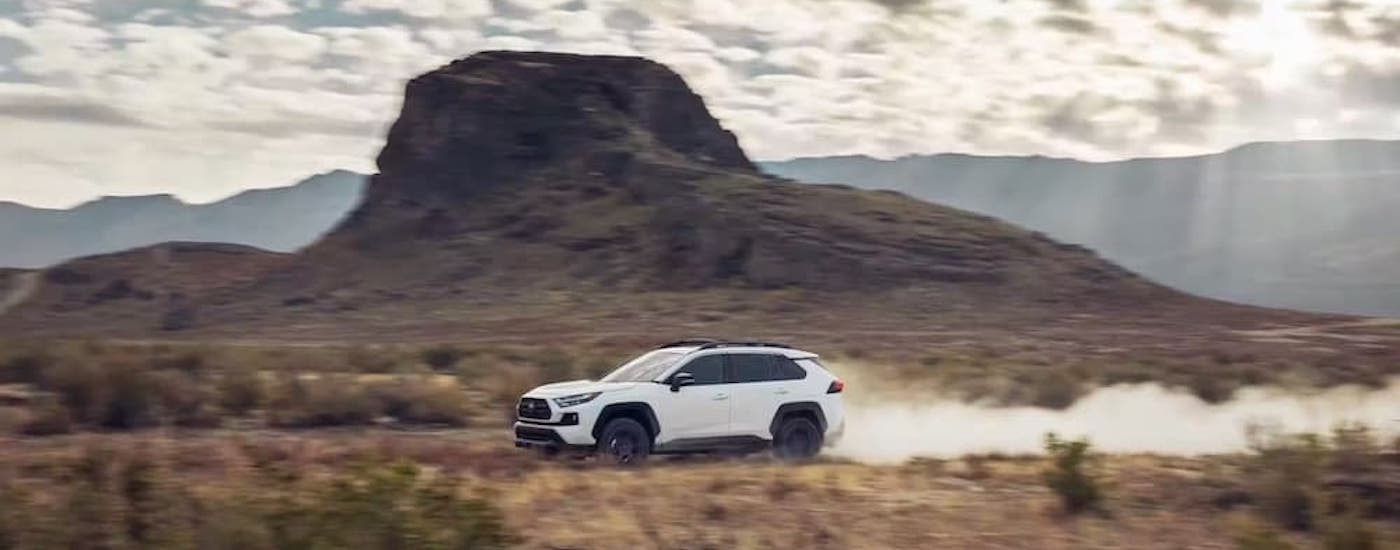 A white 2024 Toyota RAV4 for sale driving on a dirt road.