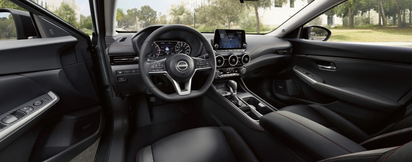 The black interior of a 2025 Nissan Sentra for sale is shown from the driver's seat.