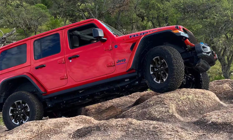 Red Jeep driving up rocky terrain