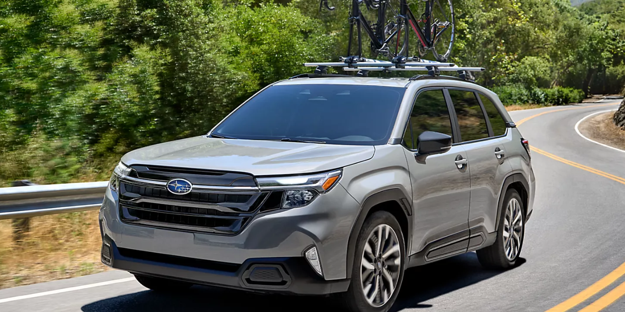 A gray 2025 Subaru Forester drives on a curvy two-lane highway