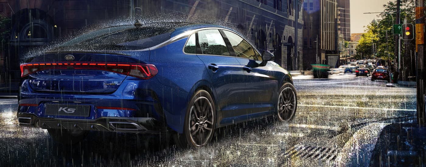 A blue 2023 Kia K5 GT is shown from the rear at a angle in the rain.