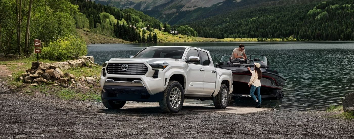 A white 2024 Toyota Tacoma for sale in San Marcos towing a boat at a lake.