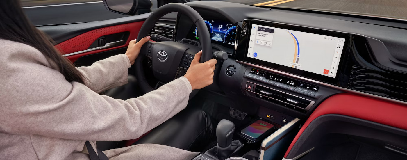 A woman driving in the red and black interior of a 2025 Toyota Camry for sale near San Antonio.