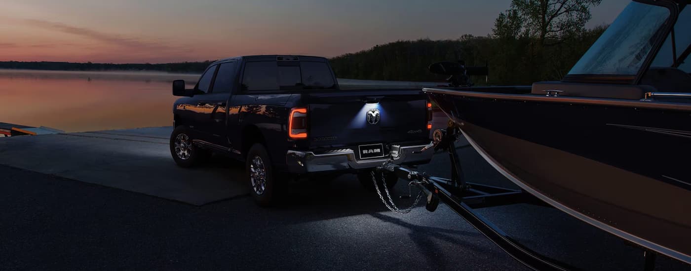 A blue 2025 Ram 2500 is towing a boat near a lake at sunset.