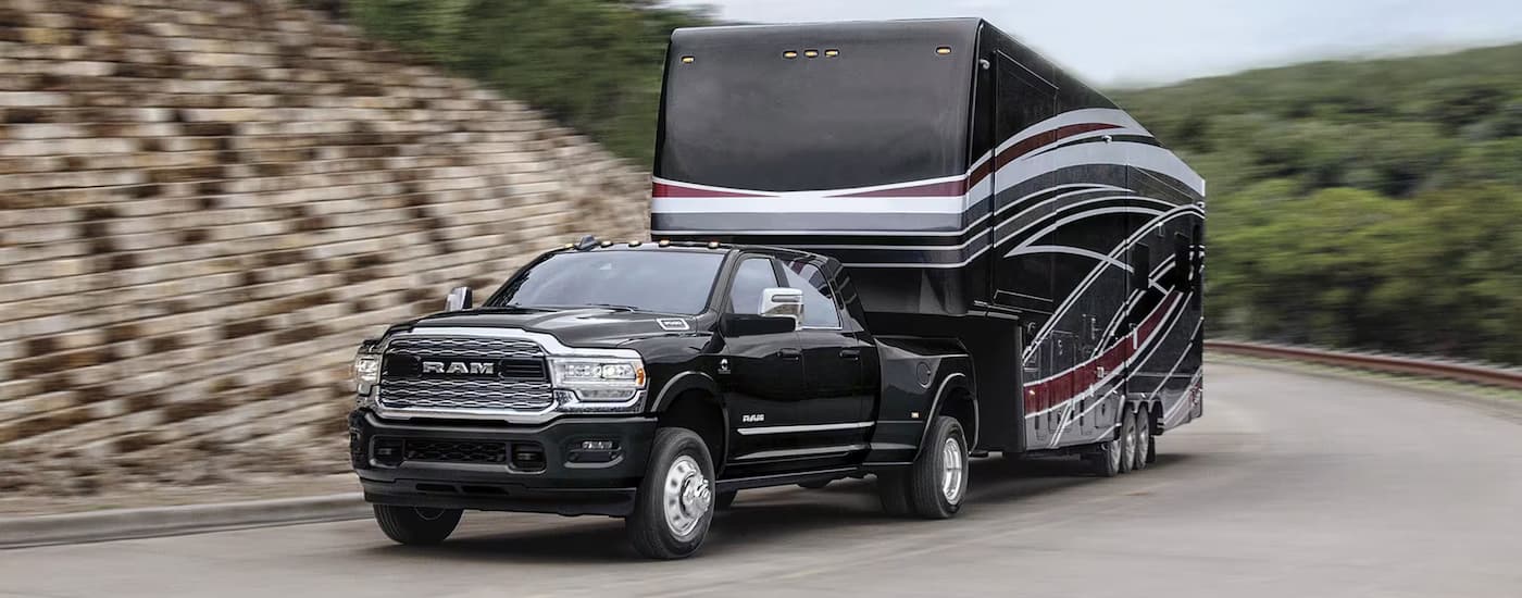 A black 2024 Ram 3500 is towing a large black camper trailer on a winding road.