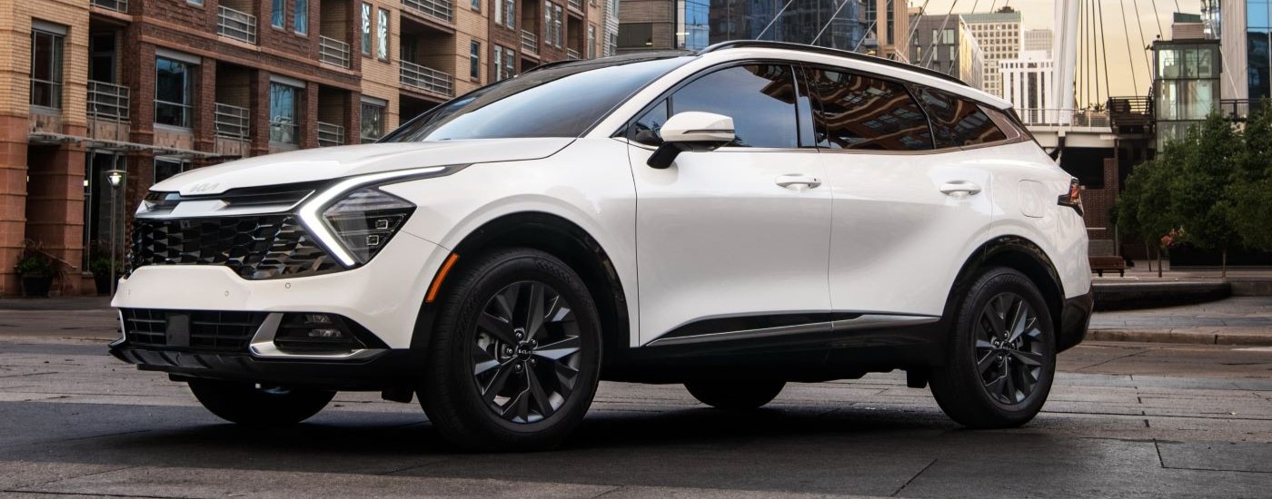 A white 2023 Kia Sportage Hybrid is driving on a city street after leaving a used Kia dealer.