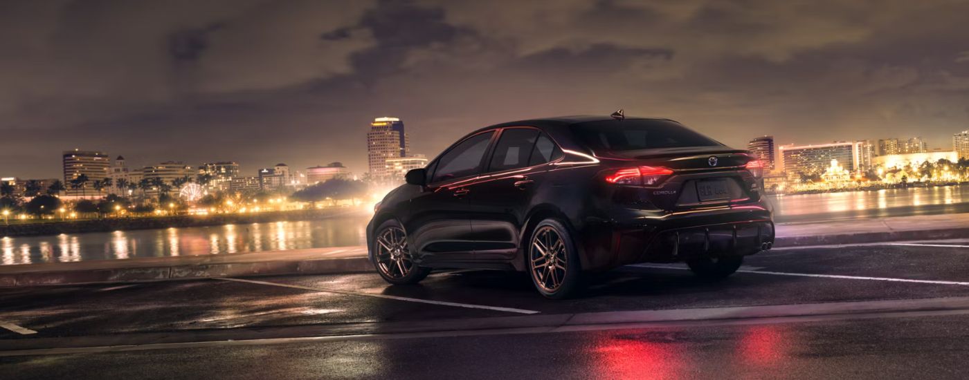 Rear view of a black 2024 Toyota Corolla Hybrid Nightshade parked overlooking city lights at night.