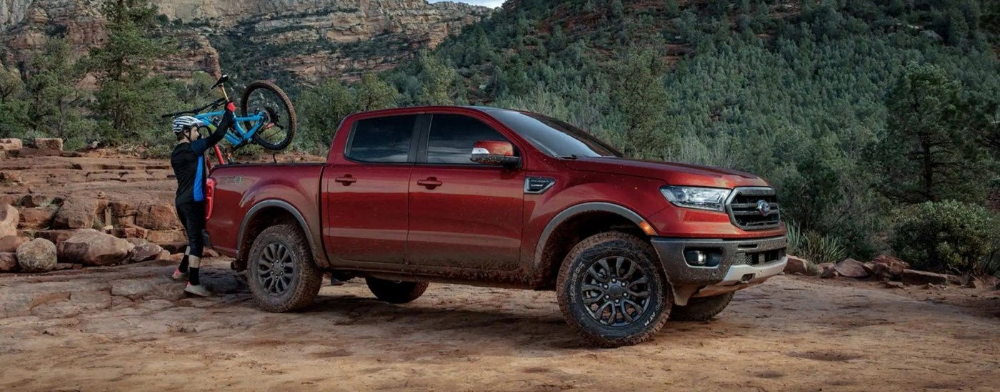 A person is shown loading a mountain bike into a maroon 2019 Ford Ranger Lariat.