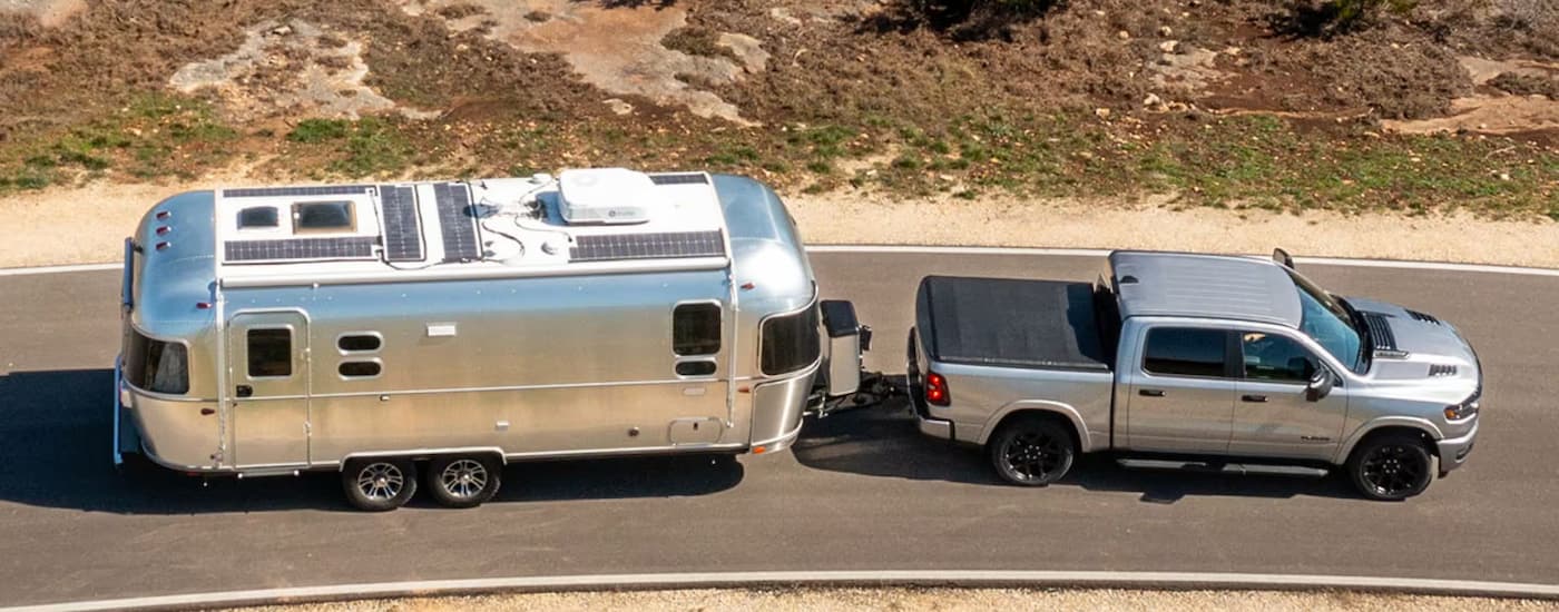 A silver 2025 Ram 1500 is towing an Airstream camper on an open road.