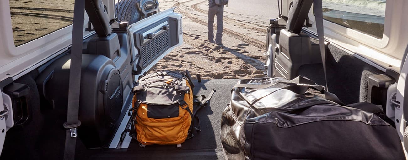 Backpacks are in the back cargo area of a 2020 Jeep Wrangler parked at a beach.