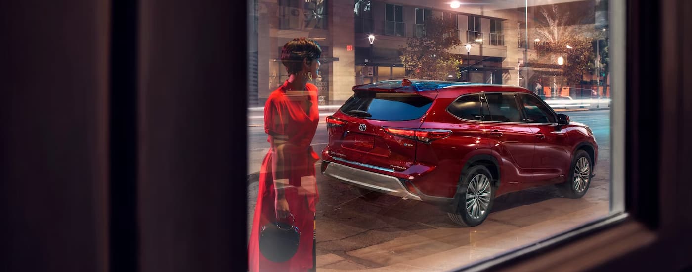 A red 2025 Toyota Highlander Platinum Hybrid is parked on the side of a city street at night.