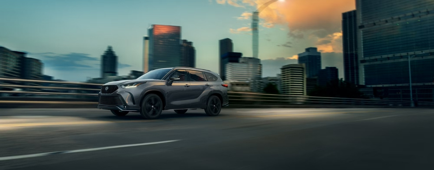 A grey 2025 Toyota Highlander for sale driving on a bridge.