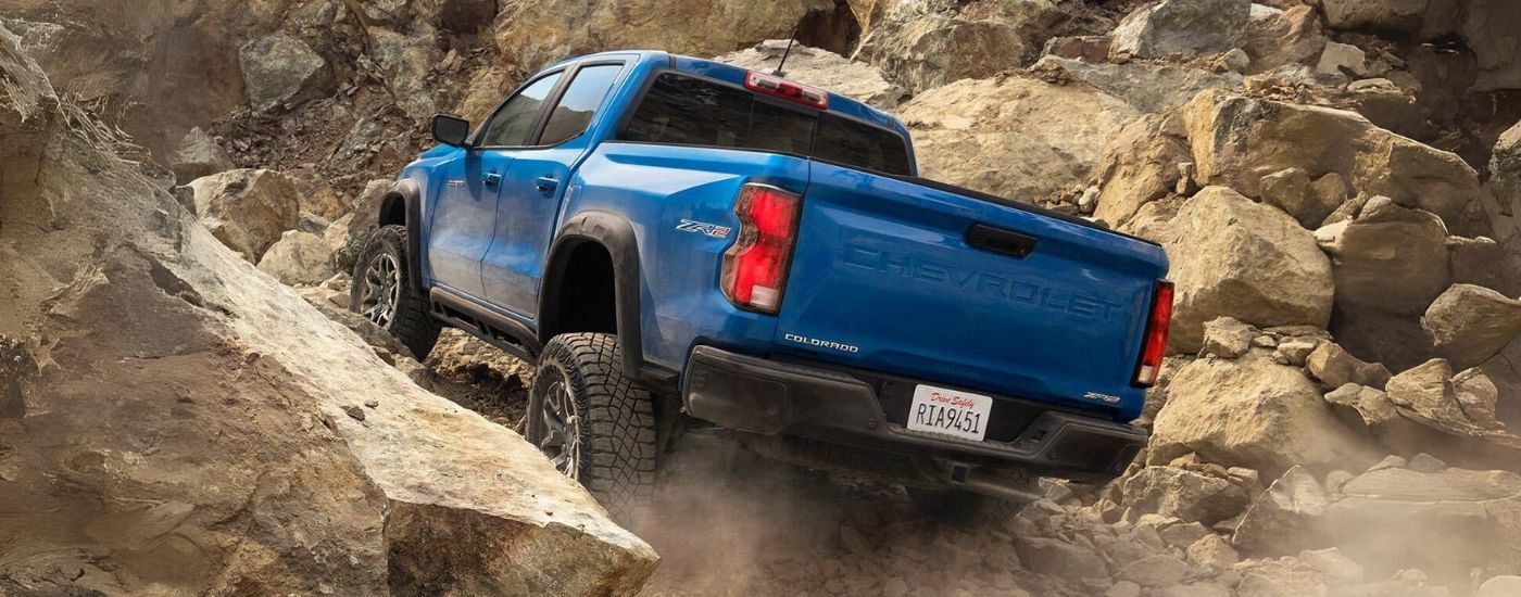 A rear view of a blue 2024 Chevy Colorado ZR2 off-roading over rocks.